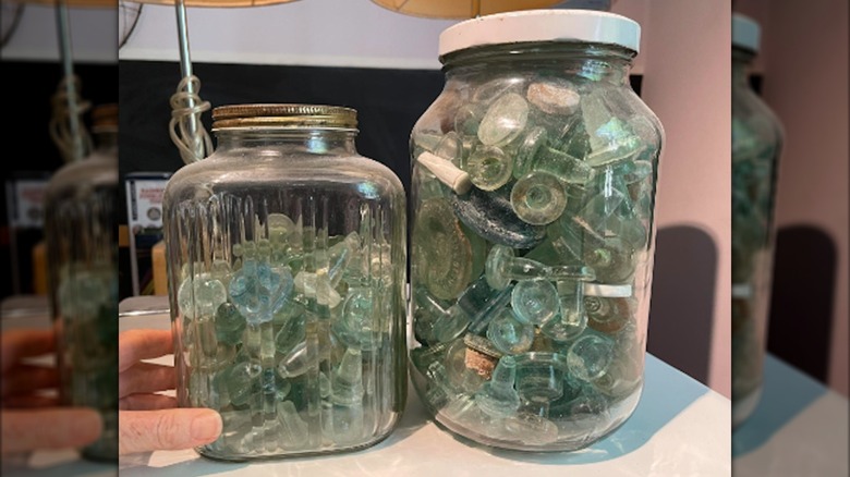 Two jars full of glass bottle stoppers with a hand holding to show jar.