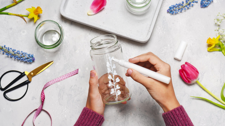 Person drawing flowers on glass jar with white marker