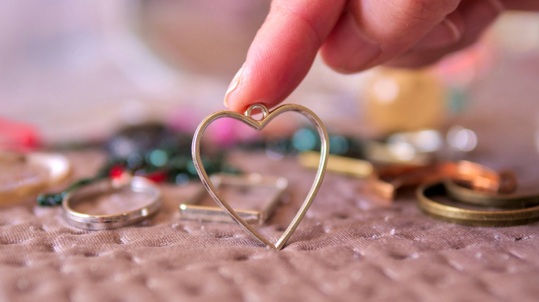 Person with finger on heart pendant with other jewelry spread around