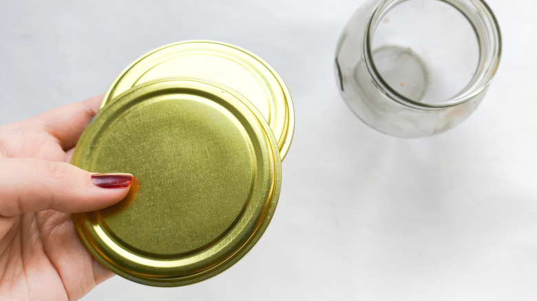 Woman holding a pair of jar lids next to a glass jar