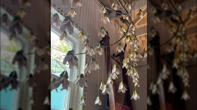 Egg carton flowers hanging off of a tree branch near a window