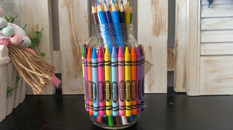 A crayon-covered glass jar with colored pencils inside