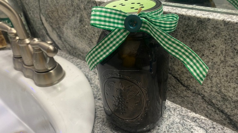 A black glass jar with a ribbon around its neck and a hole-riddled lid