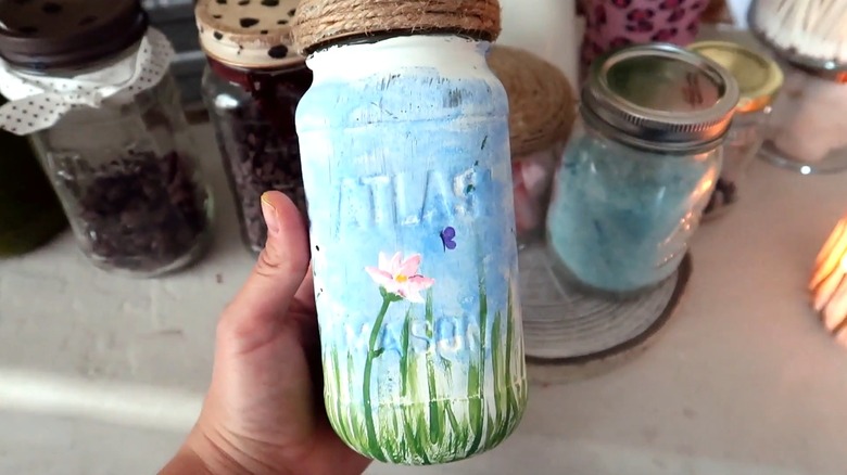 A hand holding a blue painted glass jar with twine around the neck