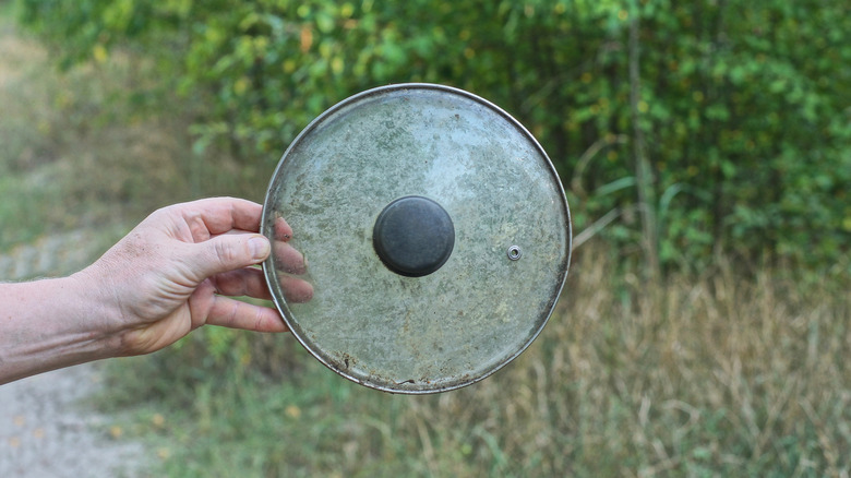 A hand holding an old glass pot lid outside
