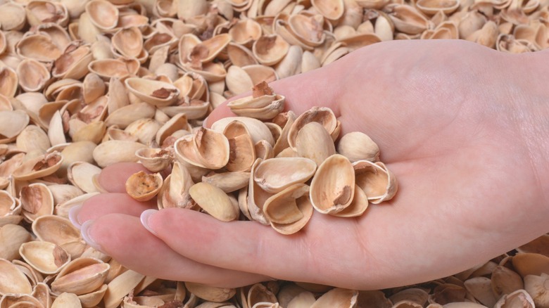 Hand scooping up empty pistachio shells from a pile