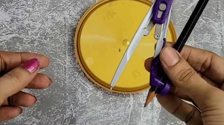 A person repurposes a lid with a pencil and compass