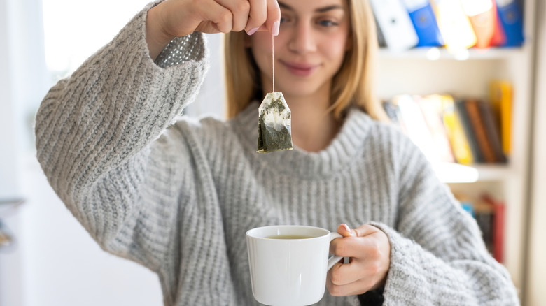 Woman holding a used tea bag and a cup of tea
