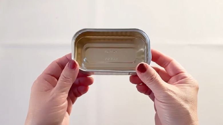 Someone holding an empty sardine can over a craft table