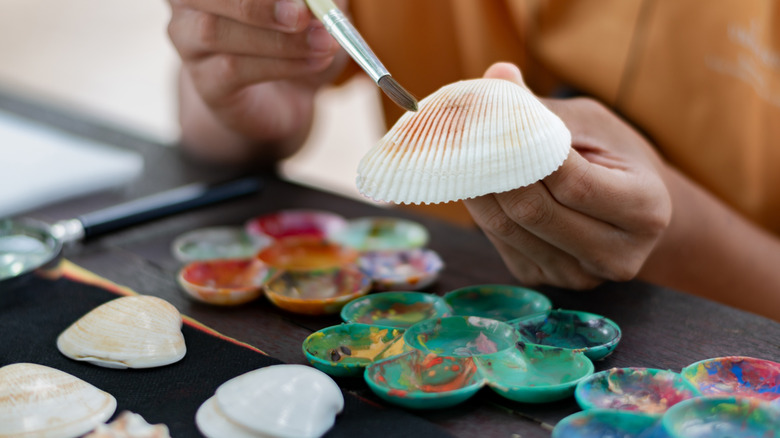 Hands painting a white seashell with a brush
