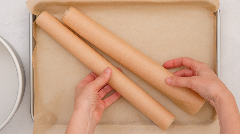 A hand rolling rolls of parchment paper on a white countertop