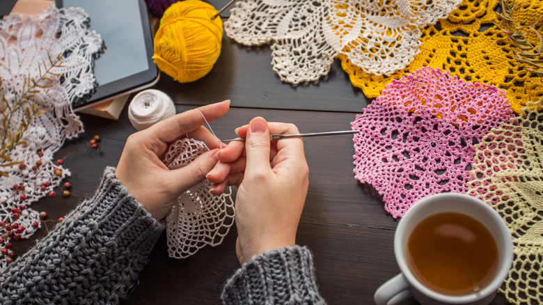 person's hand crocheting different colors of doilies with a cup of coffee on the table