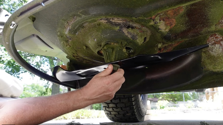 Man changing lawn mower blades from underneath elevated vehicle