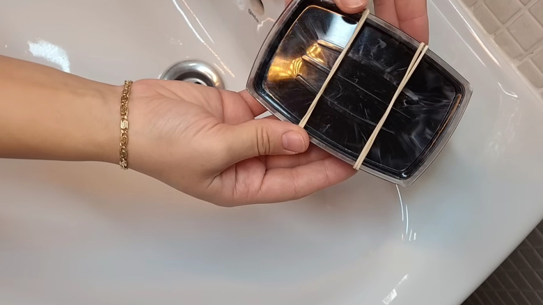 Hand tying rubber bands across a soap dish