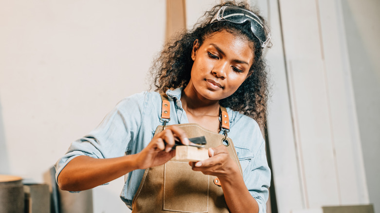 A woman uses sandpaper on a piece of wood