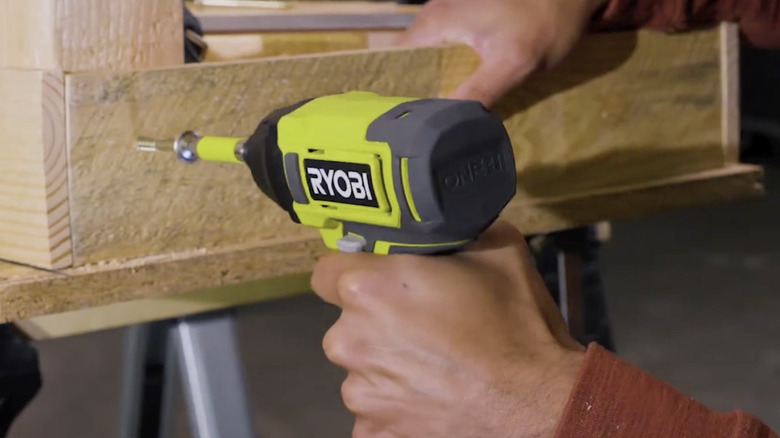 A man with a long-sleeved orange shirt using a RYOBI drill in wood