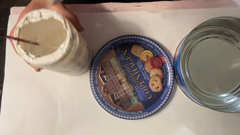 Person getting ready to paint a cookie tin to upcycle it