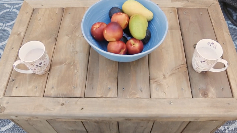 Wooden deck box serving as a table with a bowl of fruit and two mugs on top.