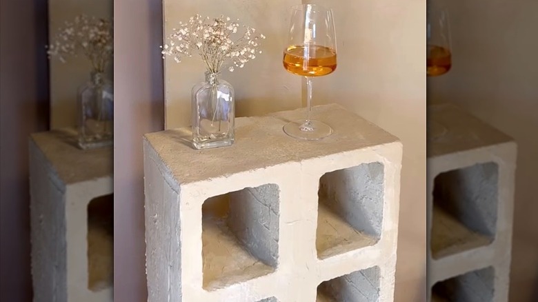 A nightstand made of concrete blocks holding a glass of wine and a small vase