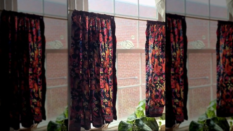Gauzy red floral pattern curtains from skirt in window, brick building seen outside