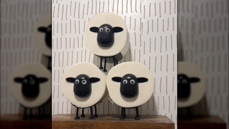 Three sheep-shaped toilet paper holders with rolls of toilet paper on them stacked on a shelf