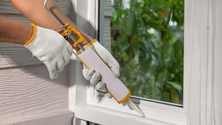 Gloved hands applying caulk to seal a window frame