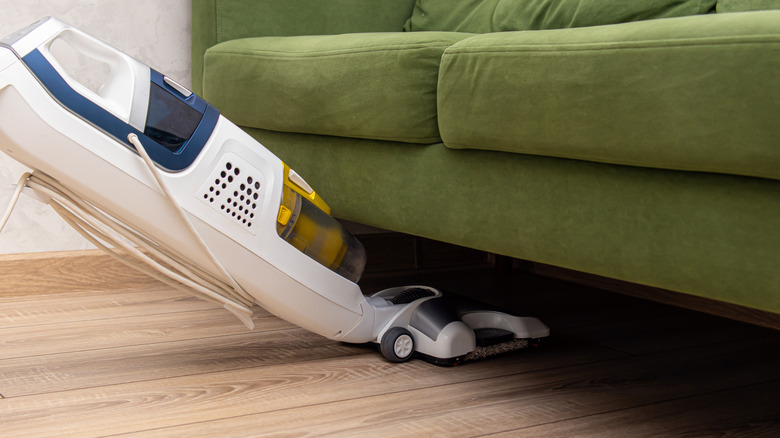 Person vacuuming under a green sofa