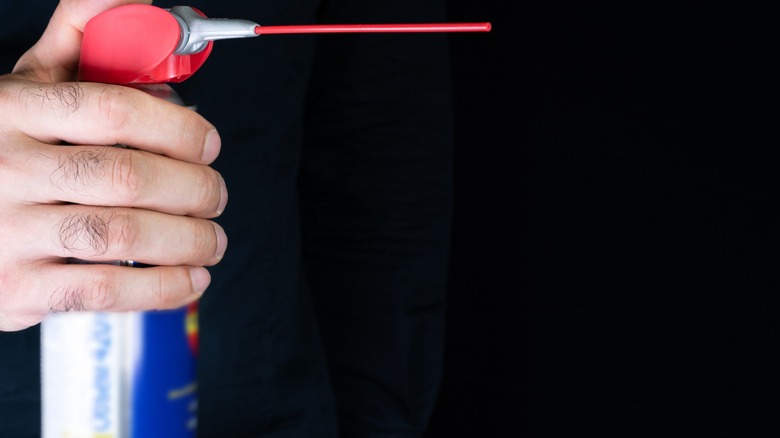 Person holding a blue aerosol can with a red straw extending from the nozzle.