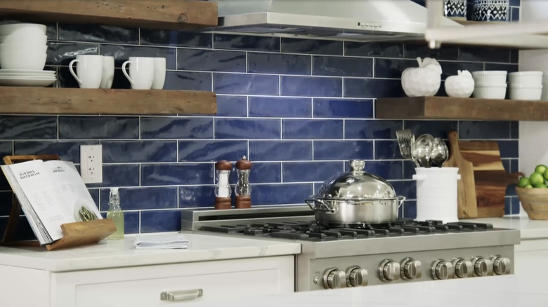 A modern kitchen's stove area with a blue glass tile backsplash
