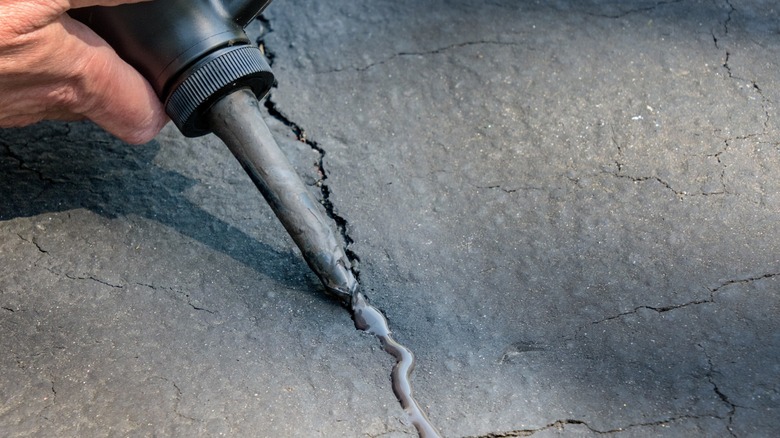 Person filling cracks in concrete with caulk; closeup of tip of caulk tube