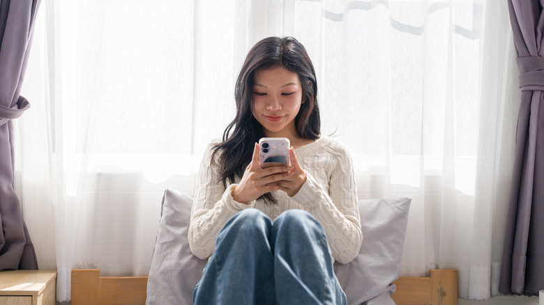 Woman looking at her phone while sitting in front of a windows