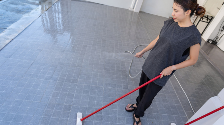 Woman cleaning garage floor with brush and hose