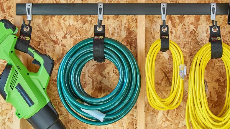 Cords, hose, and a power tool hanging from straps looped around a rod