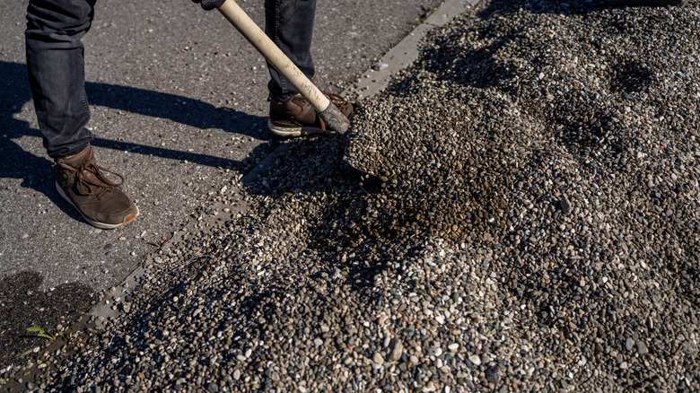 A worker shovels gravel into a driveway.