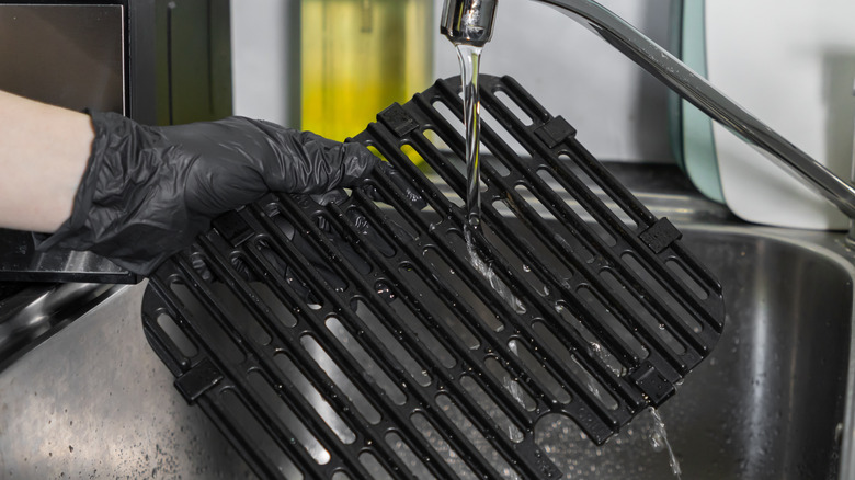 A person cleaning an air fryer grate with water in sink