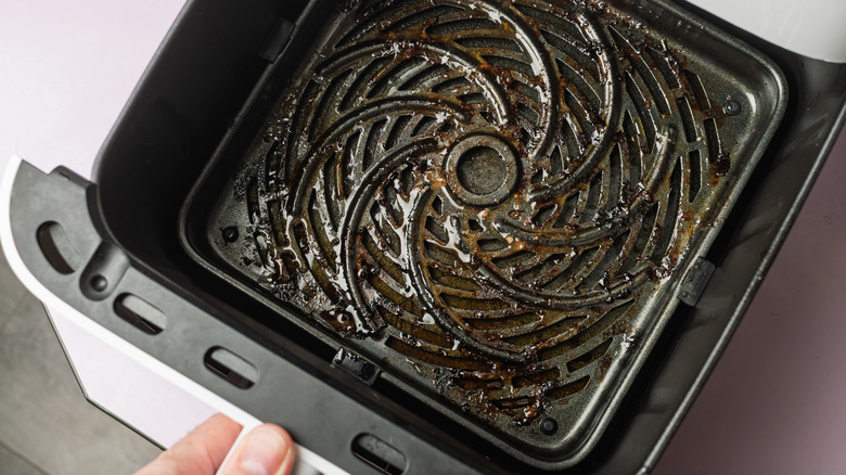 A person pulling out a greasy, dirty air fryer basket