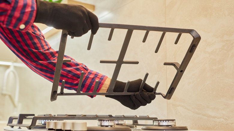 Two gloved hands lifting up a stovetop grate for cleaning