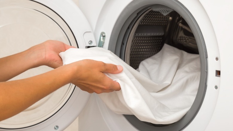 Person pulling white bed sheet from dryer