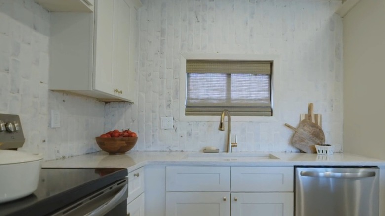 Image of kitchen with a vertical whitewashed brick backsplash, white cabinets, and white countertop.