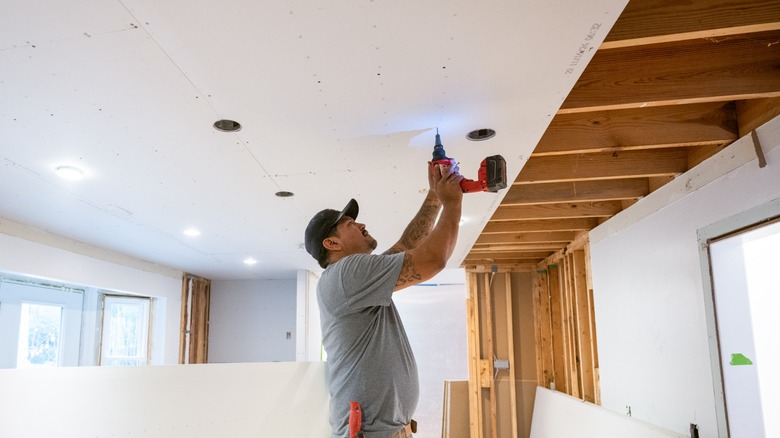 Worker fastening drywall to ceiling joists with a scew gun