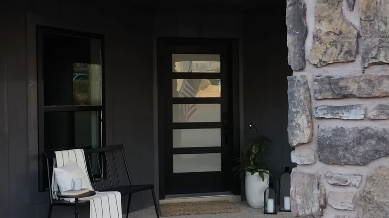 Large black metal front door surrounded by glass paneling and stone home exterior