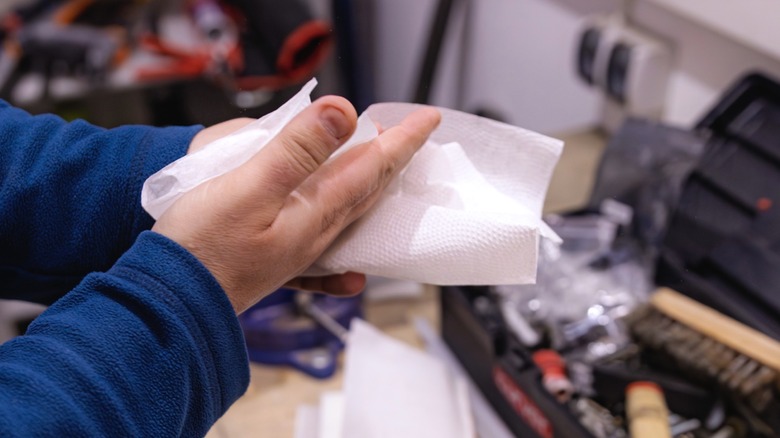 Man in front of shop workbench cleaning hands with paper towel