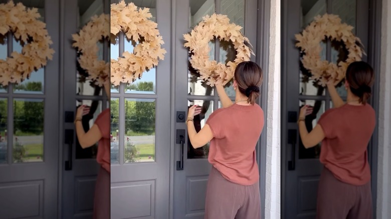 A woman hanging a burnt brown floral wreath made from a Dollar Tree pool noodle to her gray front door