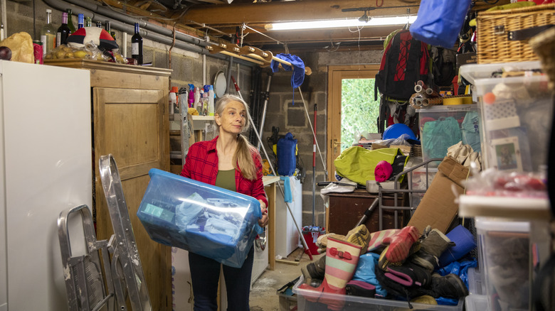 Woman carrying a plastic box in her messy garage