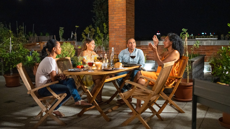 Friends chatting by a table on a lit-up patio at night