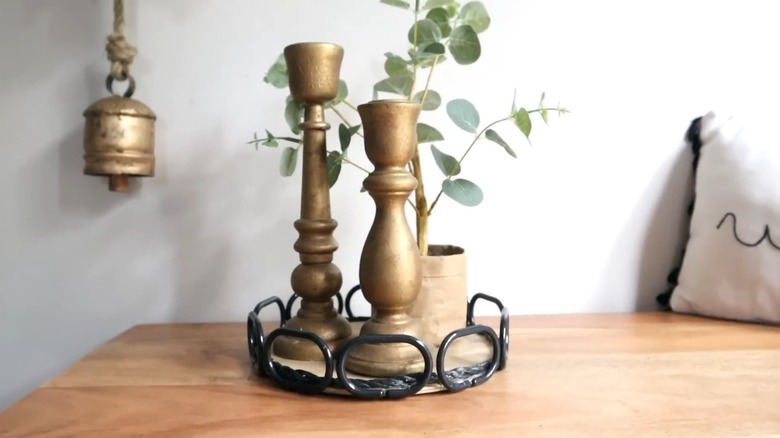 A small vase and two golden candlesticks on a round wood tray