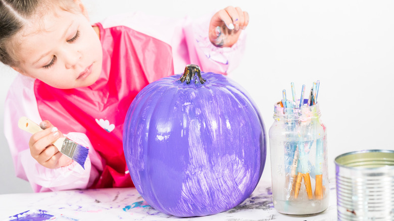 little girl painting a pumpkin purple