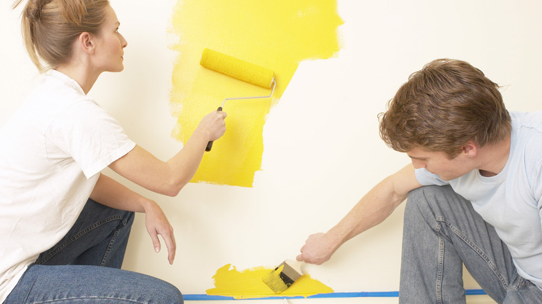 A couple paints a wall yellow