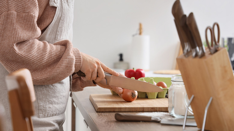 Person about to slice an unpeeled onion with a knife block in the foreground.