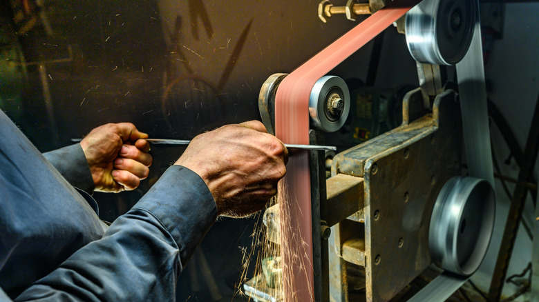 Person sharpening a lawn mower blade on a belt sander